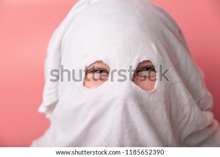 young child dressed in a ghost costume for halloween on pink background