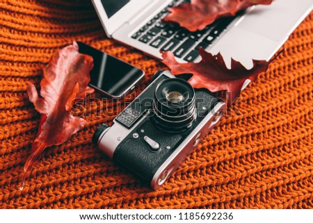 Notebook, camera and phone on orange background. Red leaves on keyboard. profession. Work place