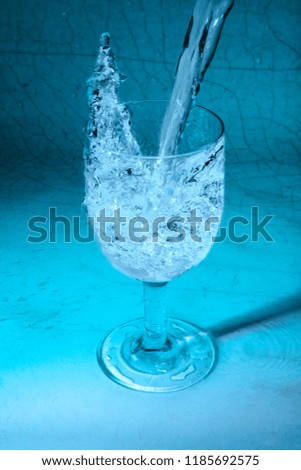 Pouring fresh water splashing from glass on turquoise and cracked background