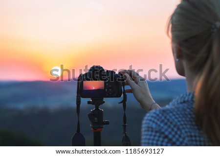 Woman is photographing sunset. Photographer with digital camera on a tripod is taking picture of landscape. 