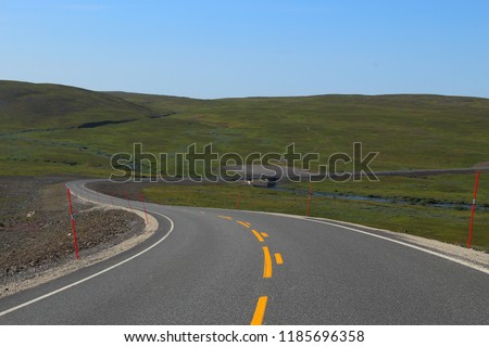 Landscape picture of a winding asphalt road with a bright orange line through flat landscape on a sunny day, near Tana in Finnmark county, Norway