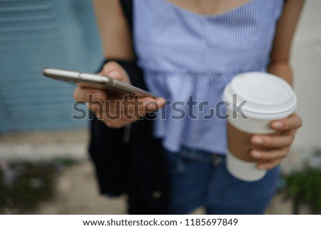Female hand using smartphone for online chat, shopping, working while holding a paper cup of coffee. Technology's impact on people's live concept. (close up, selective focus, blurred space for text)