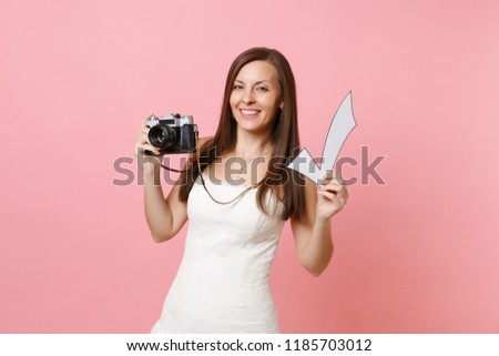 Attractive bride woman in wedding dress holding retro vintage photo camera and check mark, choosing staff, photographer isolated on pink background. Wedding to do list. Organization of celebration