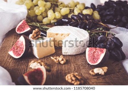Cheese soft camembert with mildew with oregano branches on a dark wooden background with grapes, fig tree and walnuts