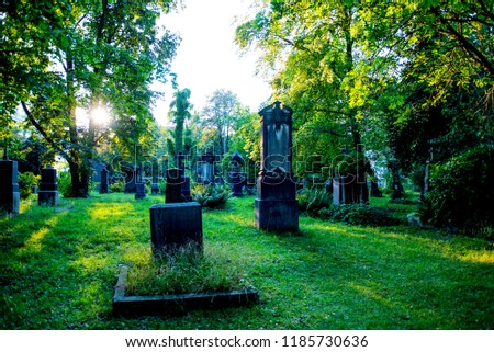 A spooky cemetery at dusk with the sun's rays streaming through the trees and gravestones