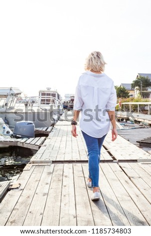 young cute blonde girl on a sunny afternoon walking along the promenade next to yachts