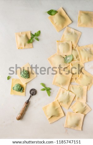 Homemade raw uncooked italian pasta ravioli staffed by spinach ricotta, basil leavrs, pasta cutter. White marble background. Flat lay, space