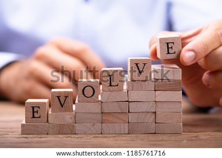 Close-up Of Person's Hand Placing Last Alphabet Of Word Evolve On Wooden Block Royalty-Free Stock Photo #1185761716