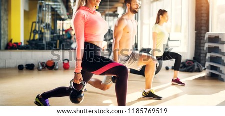 Picture of a people in a fitness class doing one leg squats with kettle bells in their hands.