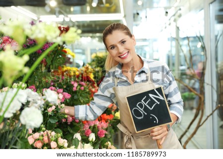 Female florist holding sign "OPEN" in flower shop