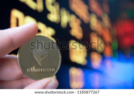 closeup fingers hold the bitcoin coin in front of stock market screen