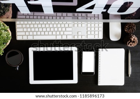Office desk with tablet and smartphone mockup on black wooden table, A top view shot.
