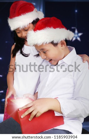 Picture of two Asian children looks astonished while opening a gift box at Christmas time. Shot at home