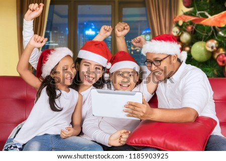 Asian family wearing Santa hat while using a digital tablet with happy expression. Shot at home