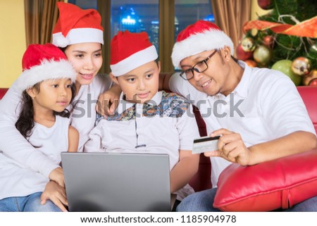 Picture of young family wearing Santa hat while using a credit card and laptop for shopping online. Shot at home