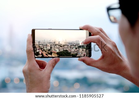Young people take pictures of the buildings in the city. Sunrise time He uses a high-angle recording photo phone.Travel concepts and technology