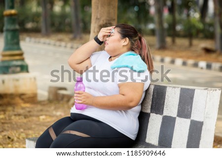 Picture of fat woman looks exhausted after doing a workout while sitting in the park