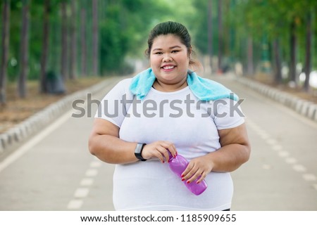 Picture of happy obese woman wearing sportswear while holding a bottle of water on the road