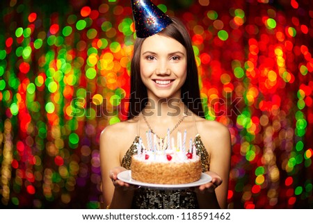 Portrait of joyful girl holding birthday cake and looking at camera at party