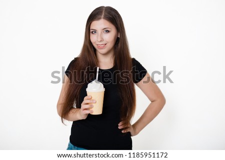 A young, beautiful girl in a black T-shirt and blue jeans is holding a glass with a straw in her hands. Studio photo on white background.
