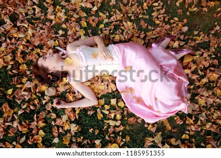 Fine emotional brunette sleep on autumn leaves and grass, top view. Yonge girl in vintage pink pastel with live expressions on beautiful country and old background.