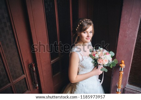 A beautiful bride stands near an old door and smiles. Wedding portrait of a young bride. Wedding photography.