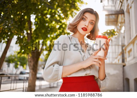 woman in a light shirt and in a red skirt holds a glass with a drink in her hand                               