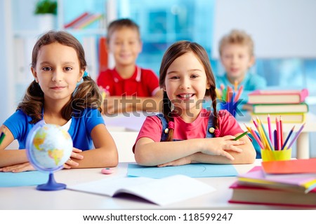 Portrait of two diligent girls looking at camera at workplace with schoolboys on background