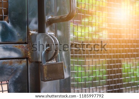 Old brass pad lock was locked metal door in restricted area with sunlight radial behind wire mesh background.