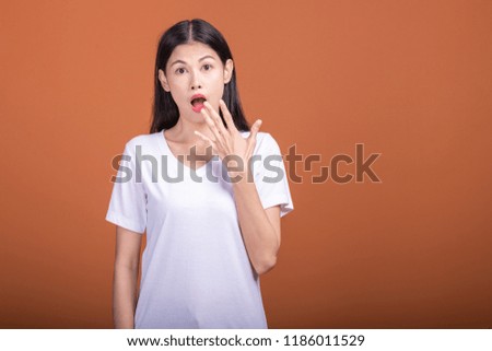 Surprise woman over orange background. Young Asian hipster woman in white t-shirt with surprise pose, hand over mouth. Young woman hipster concept.