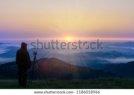 Nature photographer in work. Man silhouette above clouds, morning / evening hilly landscape. Nature, travel, tourism, extreme, healthy lifestyle, adventures. Traveler takes photos of sunrise / sunset