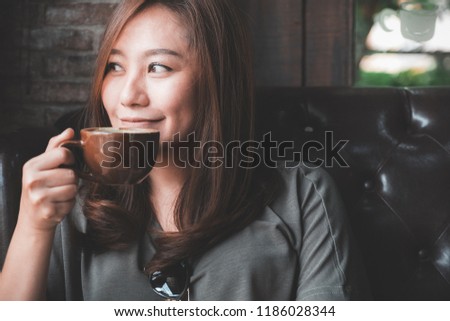 Closeup image of a beautiful Asian woman holding and drinking hot coffee with feeling good in vintage cafe