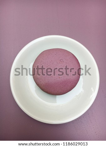 Purple french almond cake macaron on a purple table surface directly above view. Minimalistic photo in the purple tone, wallpaper, background