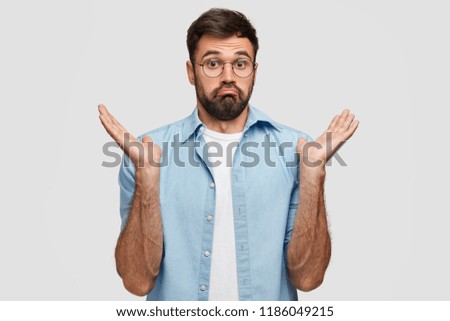 Unaware clueless bearded handsome man shrugs shoulders with uncertainty, cannot answer question, being uninterested in something, stands against white background. I dont care about it anymore Royalty-Free Stock Photo #1186049215