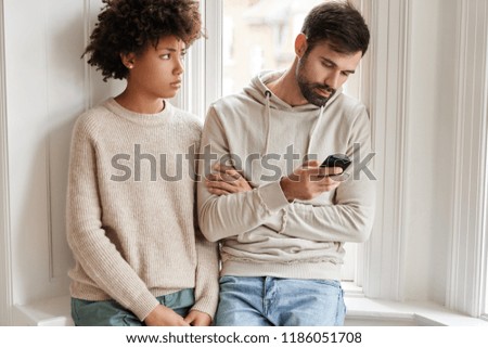 Sad African woman in oversized sweater feels displeased as being neglegted by boyfriend, needs lively communication, her husband addicted to modern technologies. Family relationships concept Royalty-Free Stock Photo #1186051708