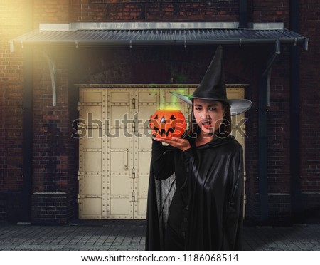 Portrait of woman in black Scary witch halloween costume holding halloween pumpkin with Old Brick Wall of the Ancient Castle of the Witch is background Vintage style Color