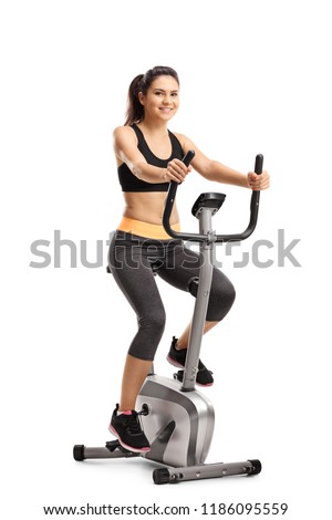 Full length portrait of a young female riding a stationary bike isolated on white background