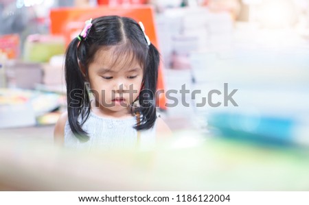 Asian child or kid girl happy reading or choose tale or story book and shopping on bookshelf in bookstore sale or library room at kindergarten school or nursery and department store for learning study