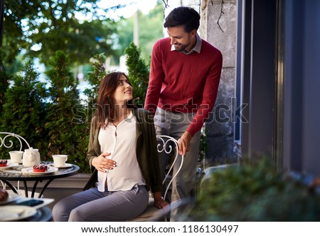 You are precious. Portrait of loving young couple having romantic date in outdoor cafe. Gentleman helping pregnant lady to sit down at the table while she is touching her belly
