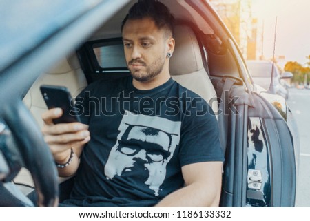 Close up of man sitting in the black car and looking at mobile phone screen.