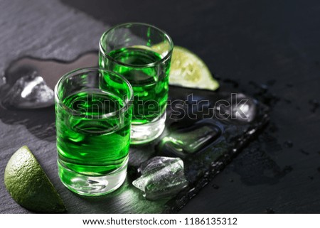Two glasses of absinthe with melted ice and slices of lime and on a black background