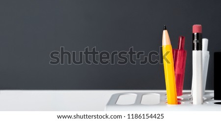 Close up yellow pencil and pen in modern white  pencil box at dark grey wall in office. copy space for adding text