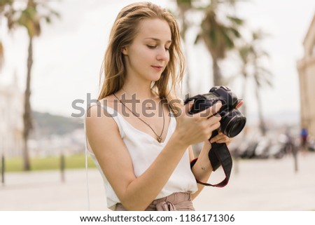 Pretty smiling girl taking pictures on dslr camera and checking the settings on the screen. Professional female photographer traveller shooting on photo camera in the park. Summer, green park outdoors