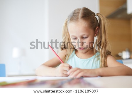 Pretty serious girl drawing picture with crayons at leisure while staying at home