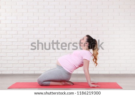 Young pregnant woman doing exercises on brick wall background