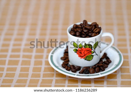 Coffee cup with a red rose drawn is filled with roasted beans.