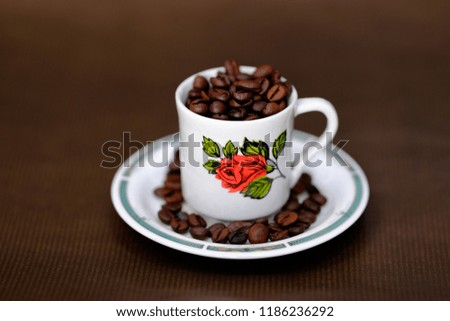 Coffee beans in mug with red rose on brown background.