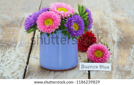 Buenos dias (good morning in Spanish) card with colorful daisies in blue vase on rustic wooden surface
