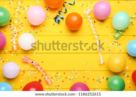 Colorful balloons with confetti on yellow wooden table