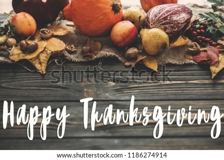 Happy Thanksgiving Text on beautiful composition of Pumpkin, autumn vegetables with colorful leaves,acorns,nuts, berries on wooden rustic table. Seasons greeting card